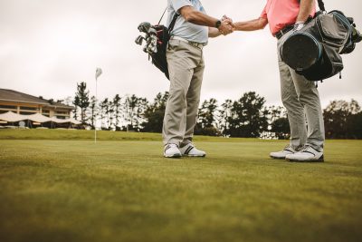 Two senior men shaking hands when meeting on a golf course.